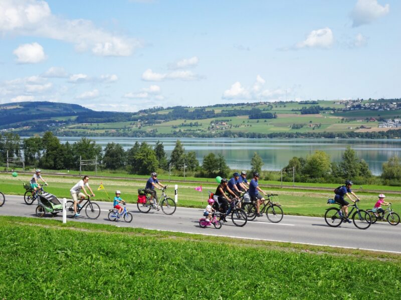 Familien und Kinder fahren mit Fahrrädern entlang eines Sees.