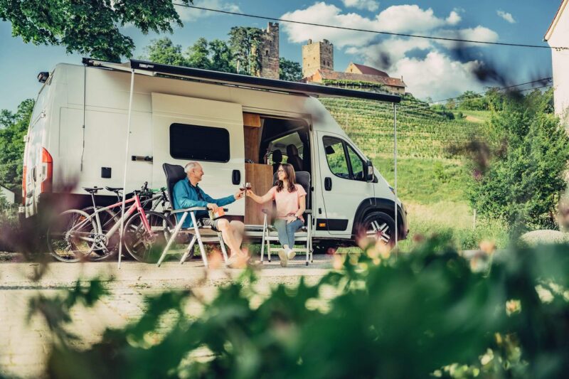 Paar entspannt vor einem Wohnmobil in der Natur.