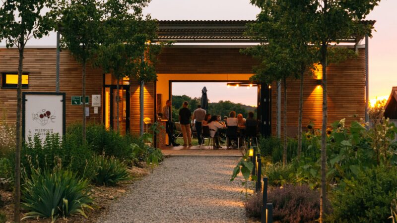 Moderne Weinbar mit Gästen im Freien, umgeben von Pflanzen.