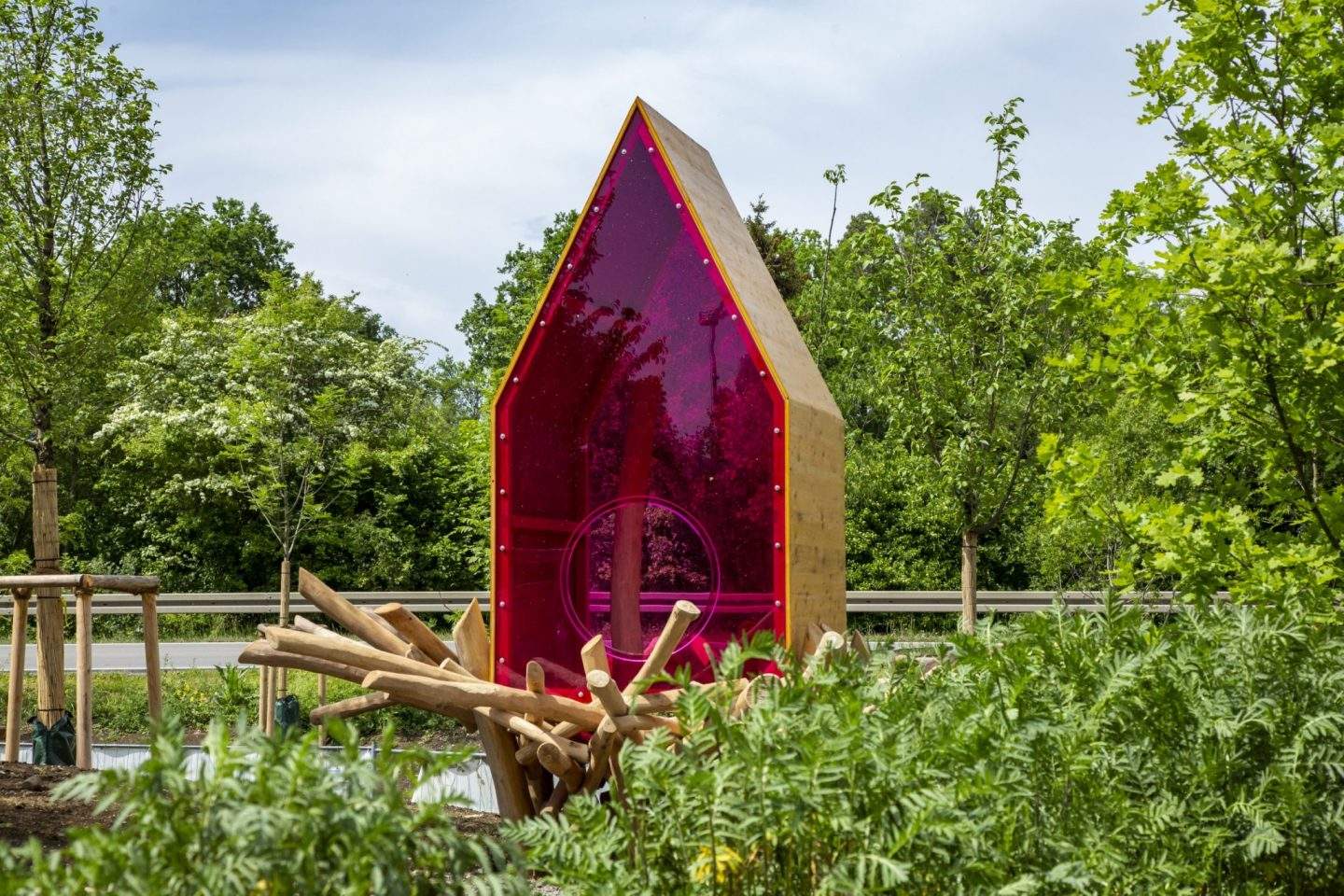 Bunte Spielstruktur in einem Park mit Holzstämmen und grünen Pflanzen.
