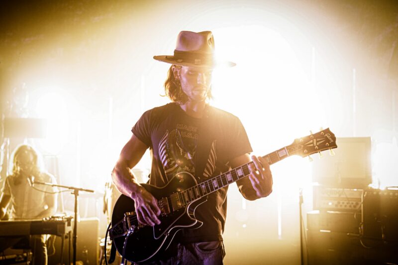 Mann mit Gitarre auf der Bühne, beleuchtet von hellem Licht.