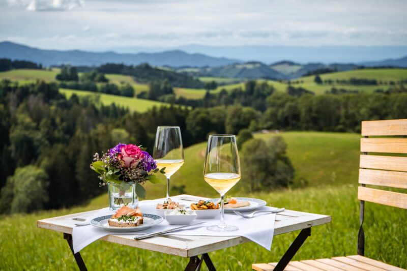 Tisch mit Essen und Getränken in einer ländlichen Umgebung mit Bergen im Hintergrund.