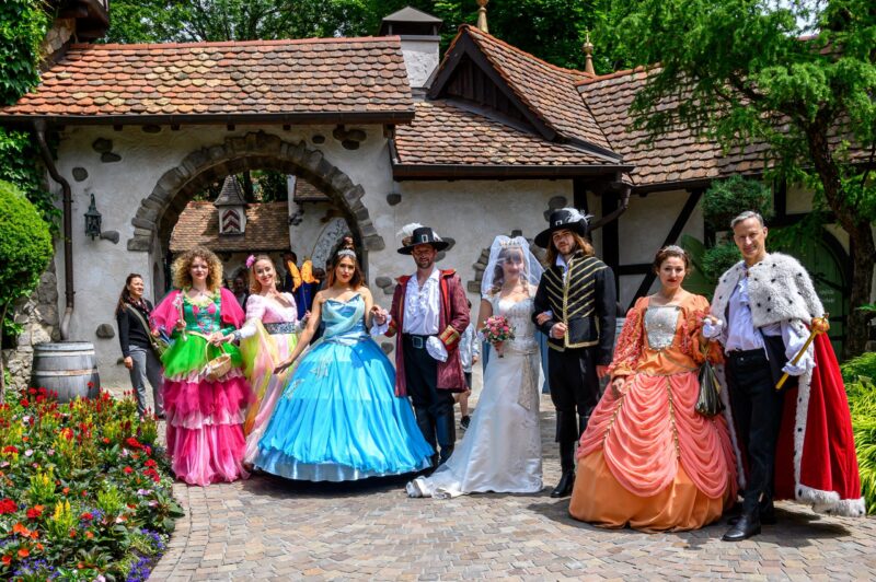 Gruppe von Menschen in historischen Kostümen vor einem Gebäude mit Ziegeldach.