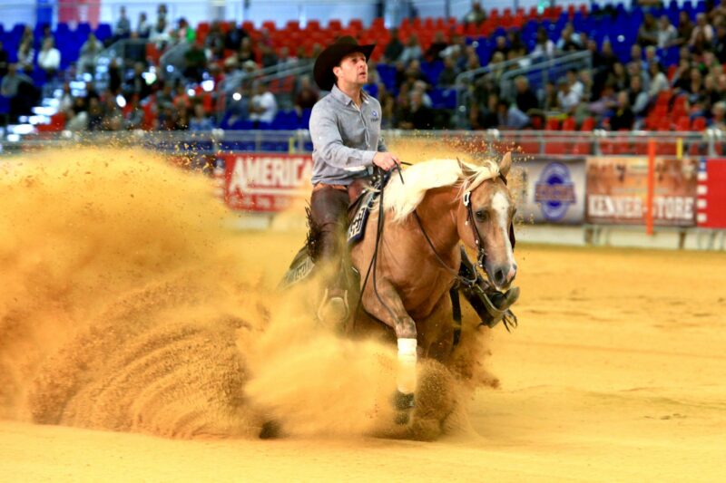 Reiter in Cowboyhut reitet auf Pferd und wirbelt Sand auf.