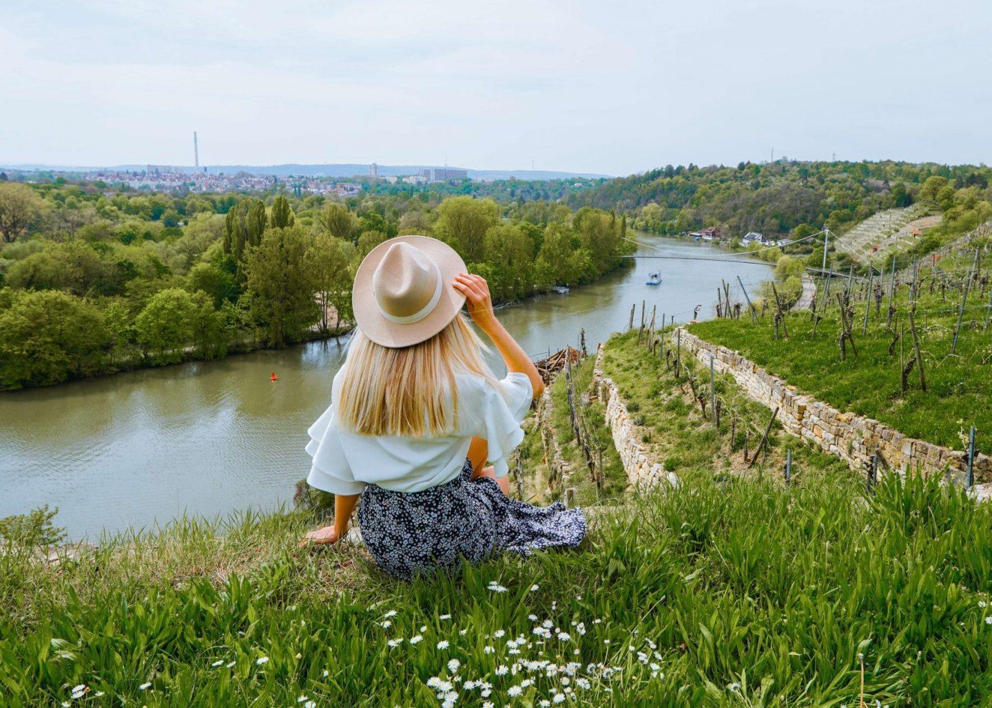 Frau mit Hut sitzt am Flussufer und genießt die Aussicht auf die Landschaft.