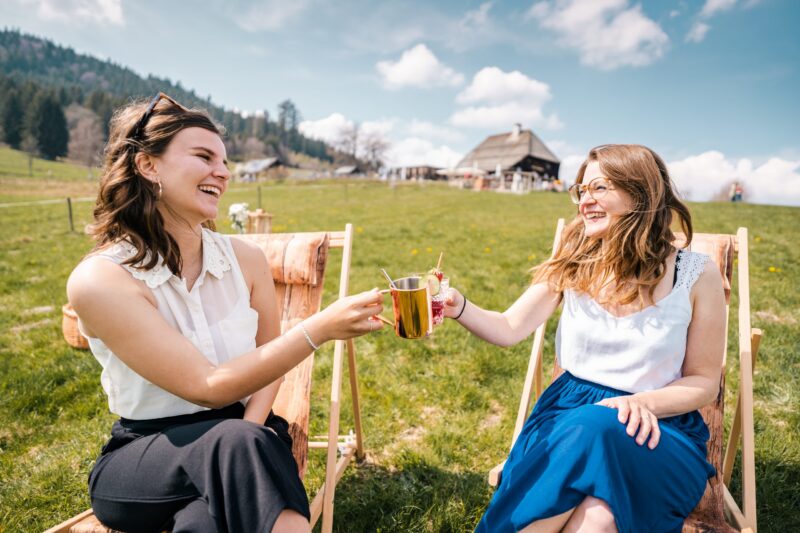 Zwei Frauen stoßen mit Getränken in der Natur an.