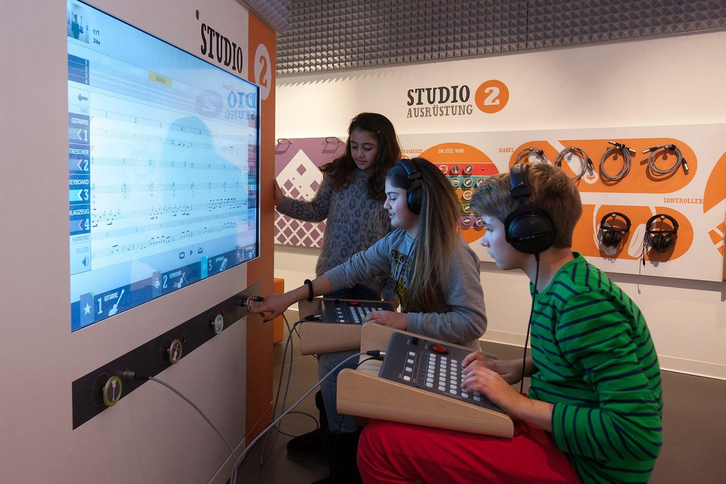 Drei Kinder arbeiten an einem Musikstudio-Computer mit Headsets.