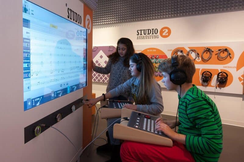 Drei Kinder arbeiten an einem Musikstudio-Computer mit Headsets.