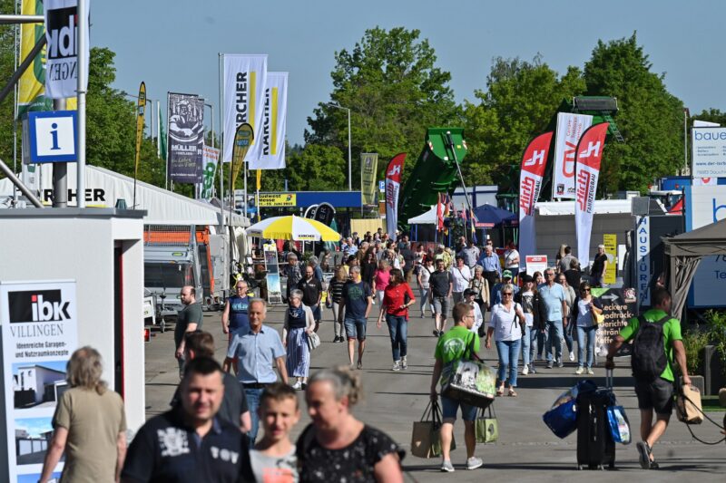 Menschenmenge auf einer Messe mit Ständen und Werbebannern.
