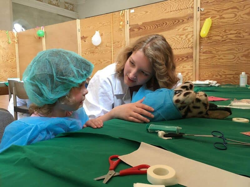Eine Frau spricht mit einem Kind über ein Stofftier in einem medizinischen Setting.