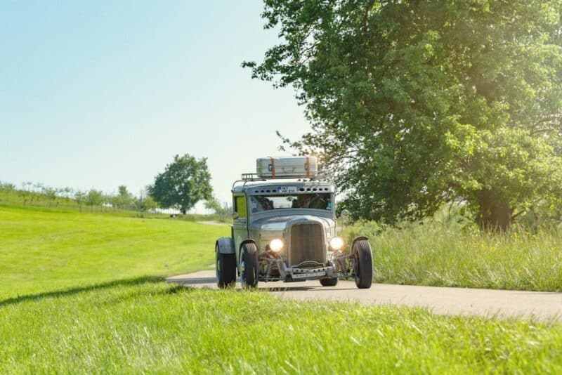 Oldtimer fährt auf einer Landstraße durch eine grüne Landschaft.