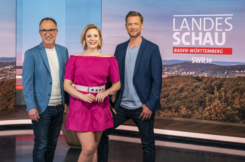 Drei Moderatoren stehen vor einem Hintergrund mit dem Schriftzug 'Landesschau Baden-Württemberg'.
