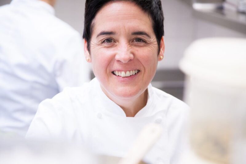 Lächelnde Köchin in weißer Kochjacke in einer Küche.