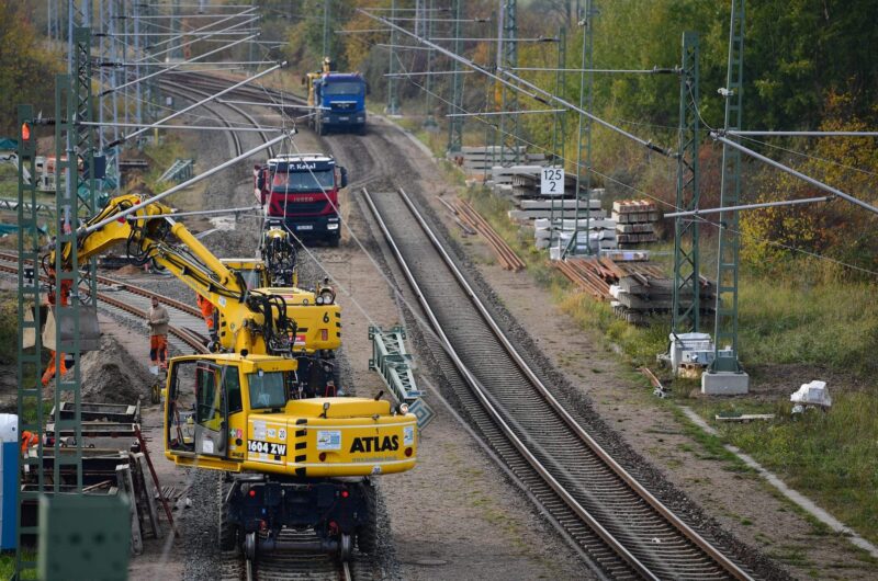 Bauarbeiten an Bahngleisen mit gelbem Kran und Lkw im Hintergrund.