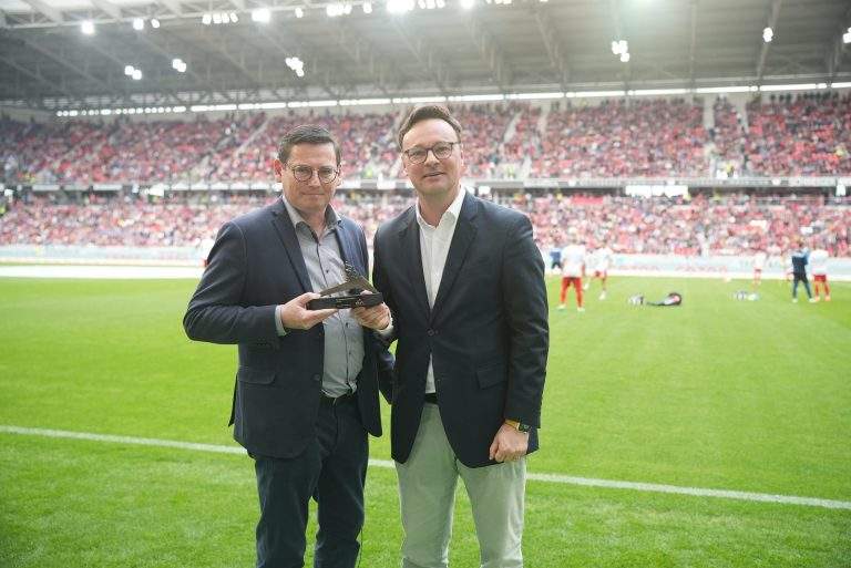 Zwei Männer stehen auf dem Fußballfeld und halten eine Auszeichnung.