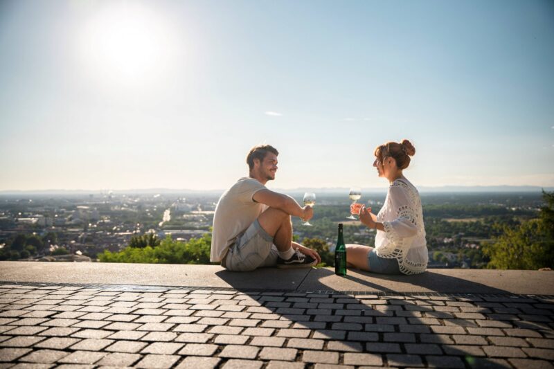 Paar sitzt auf einer Mauer und genießt Getränke mit Blick auf die Landschaft.