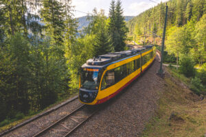 Gelbe Straßenbahn fährt durch eine bewaldete Landschaft.