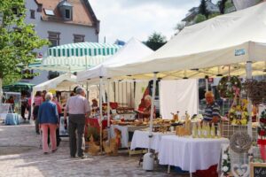 Markt mit Ständen und Besuchern an einem sonnigen Tag.
