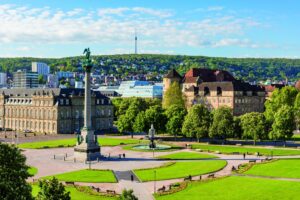 Blick auf einen Park mit Denkmal und historischen Gebäuden im Hintergrund.