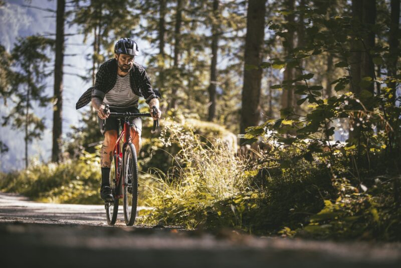 Mann auf einem Fahrrad in einem Waldweg, umgeben von Bäumen und Pflanzen.