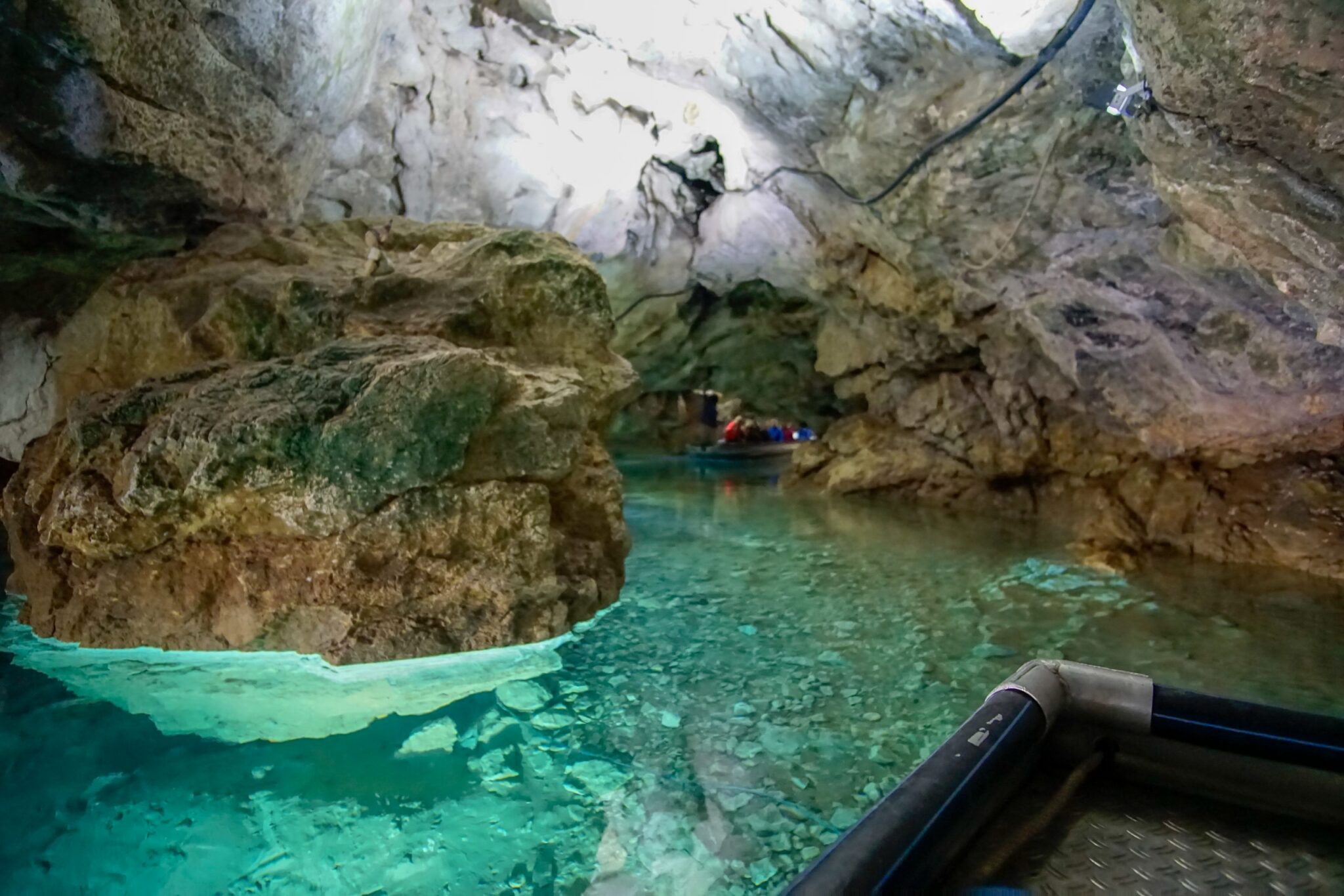 Blick auf klares Wasser in einer Höhle mit Felsen und Booten im Hintergrund.