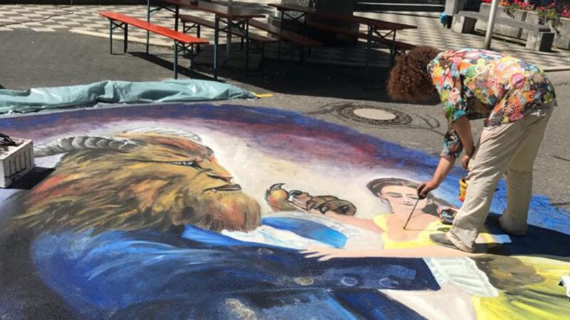 Künstler malt ein großes Wandgemälde auf dem Boden mit einer Figur und einem Tier.