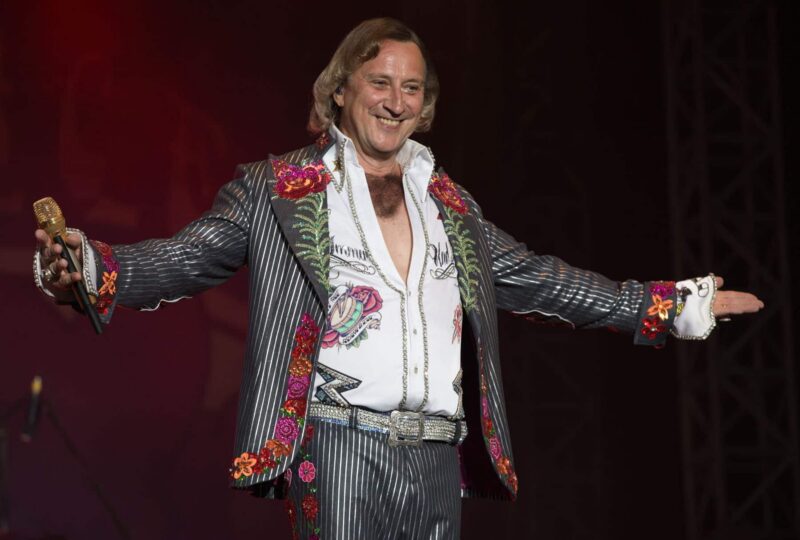 Mann in buntem Anzug mit Mikrofon auf der Bühne.