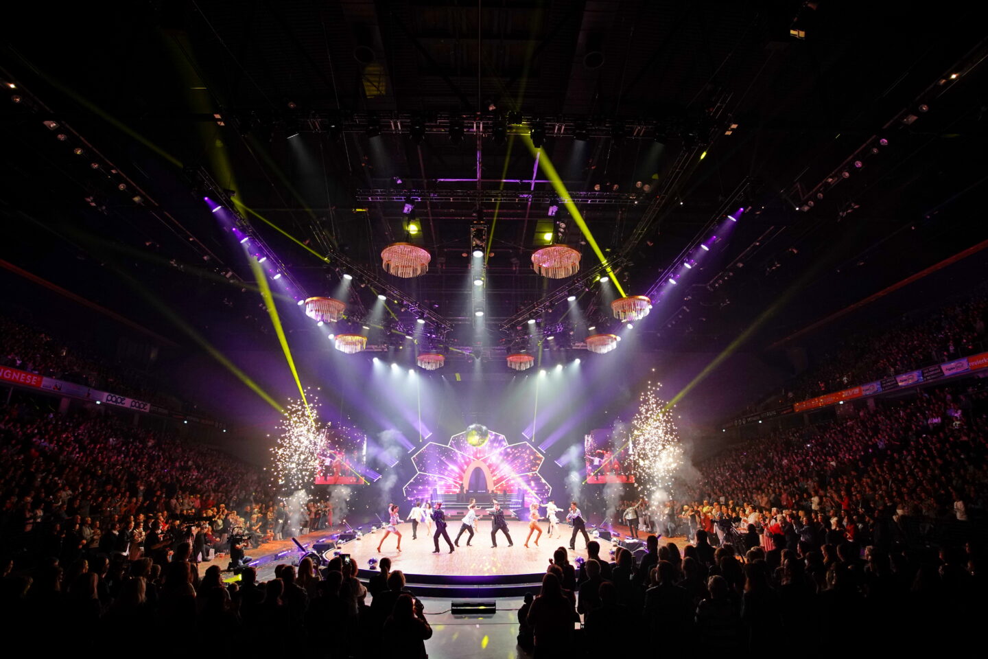 Bühne mit Tänzern und Lichtern bei einem Live-Event vor großem Publikum.