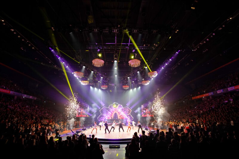 Bühne mit Tänzern und Lichtern bei einem Live-Event vor großem Publikum.