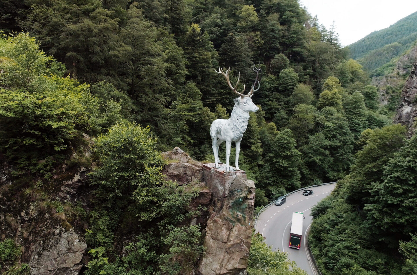 Weiße Hirschstatue auf einem Felsen in einer bewaldeten Umgebung.