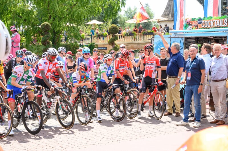 Radfahrer stehen an der Startlinie eines Rennens in einer festlichen Umgebung.
