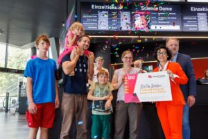 Familie feiert mit Konfetti und einem großen Ticket in einem modernen Gebäude.