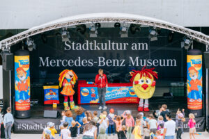 Bühne mit Maskottchen und Kindern beim Event am Mercedes-Benz Museum.