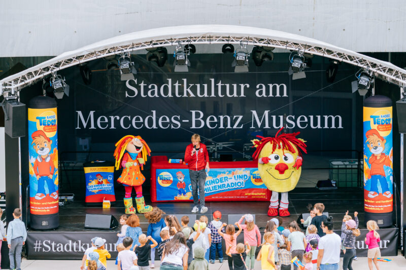 Bühne mit Maskottchen und Kindern beim Event am Mercedes-Benz Museum.