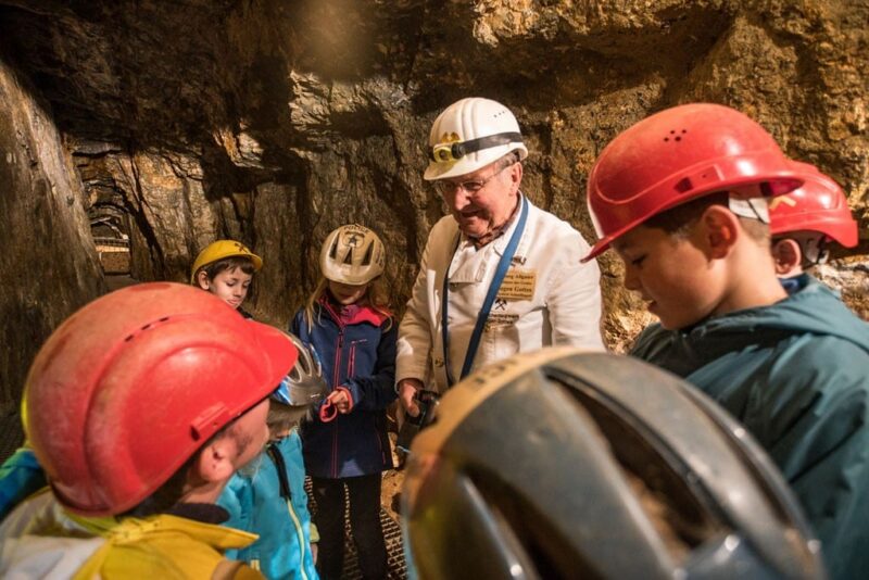 Gruppe von Kindern und einem Mann in einem Bergwerk, alle mit Helmen.
