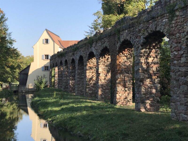 Historische Steinbrücke mit Bögen und angrenzendem Gebäude.