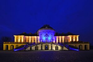 Beleuchtetes historisches Gebäude bei Nacht mit Treppen und Bäumen im Vordergrund.