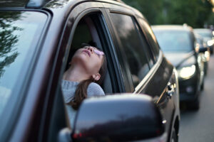 Junge Frau lehnt erschöpft aus dem Fenster eines Autos im Stau.