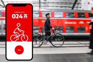Mann mit Fahrrad an einem Bahnhof, Smartphone mit App im Vordergrund.