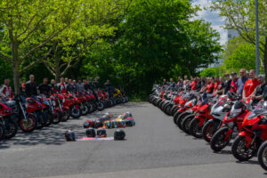 Gruppierung von Motorradfahrern mit roten Motorrädern und Helmen in einem Park.