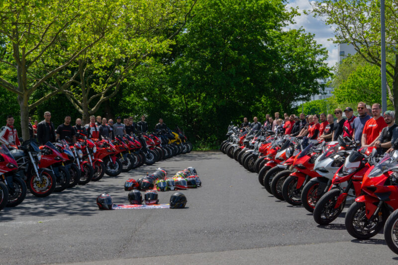Gruppierung von Motorradfahrern mit roten Motorrädern und Helmen in einem Park.