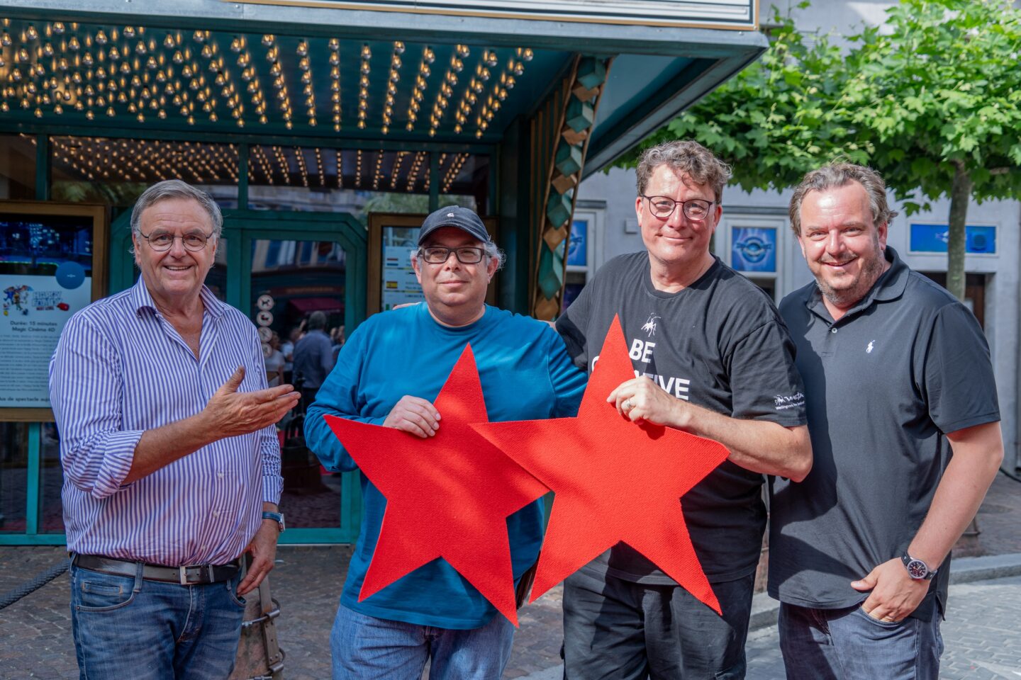 Vier Männer halten rote Sterne vor einem Theater.