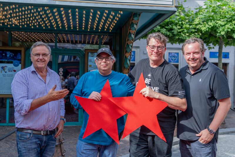 Vier Männer halten rote Sterne vor einem Theater.