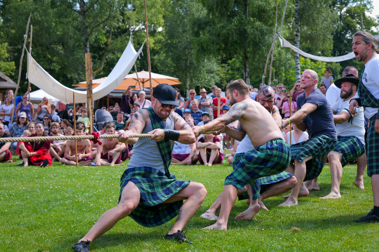 Männer im Kilt ziehen an einem Seil während eines Wettbewerbs vor Publikum.