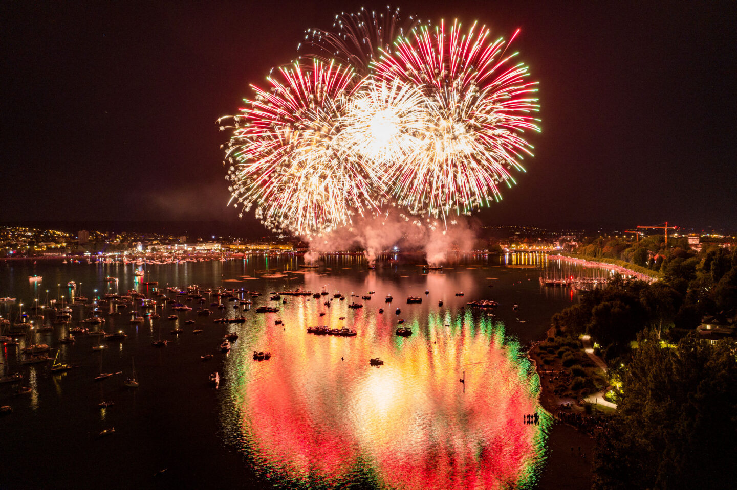 Feuerwerk über einem Gewässer mit Booten und reflektierenden Lichtern.