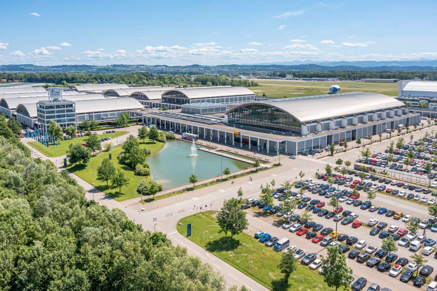 Luftaufnahme eines modernen Messegeländes mit Parkplatz und Teich.