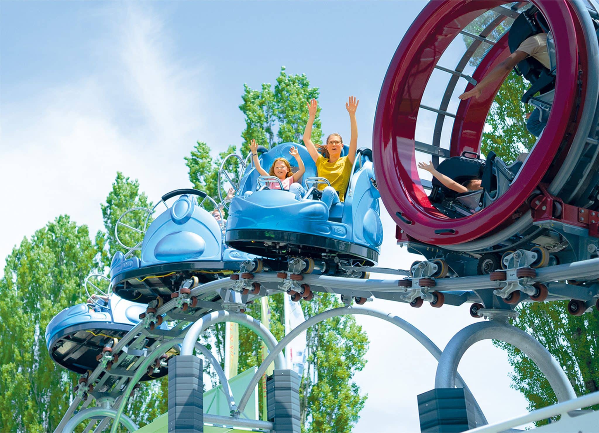 Familie auf einer Achterbahn mit erhobenen Händen, umgeben von Bäumen.