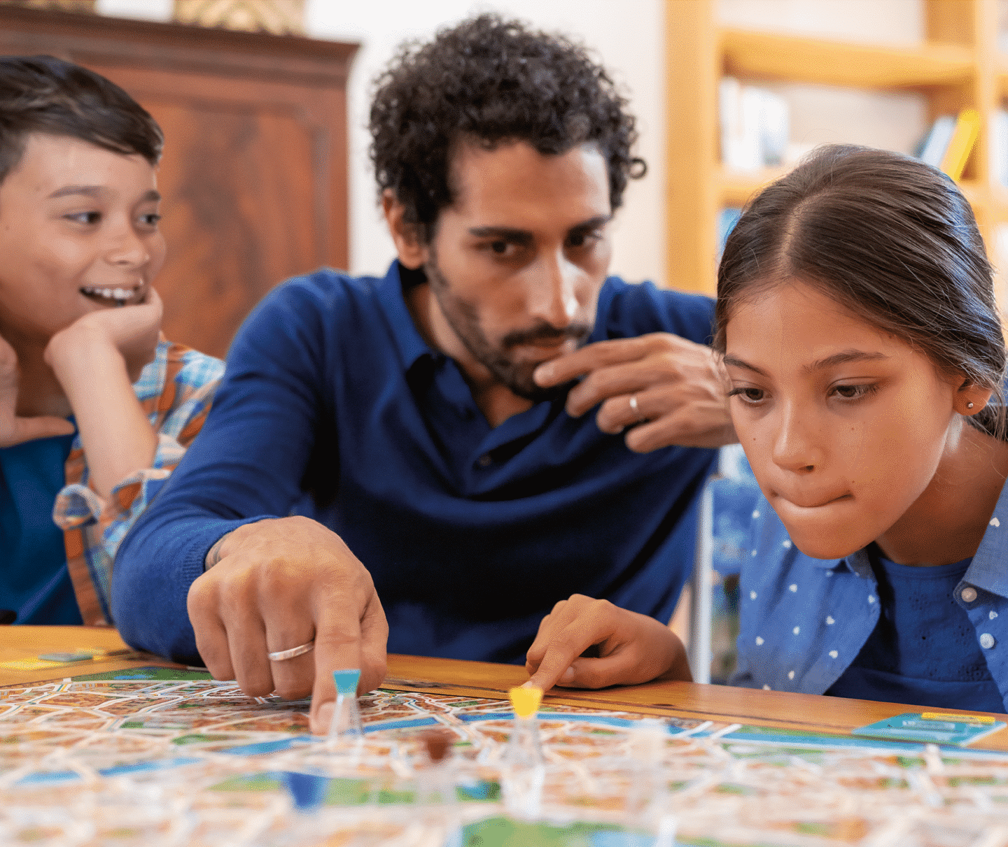 Familie spielt ein Brettspiel am Tisch, konzentrierte Gesichter.