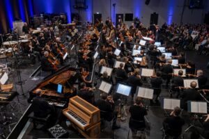 Orchester bei einem Konzert mit verschiedenen Instrumenten und Musikern auf der Bühne.