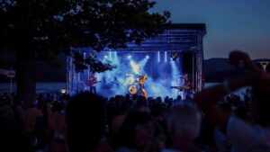 Musikveranstaltung mit Band auf einer Bühne, umgeben von Publikum bei Dämmerung.